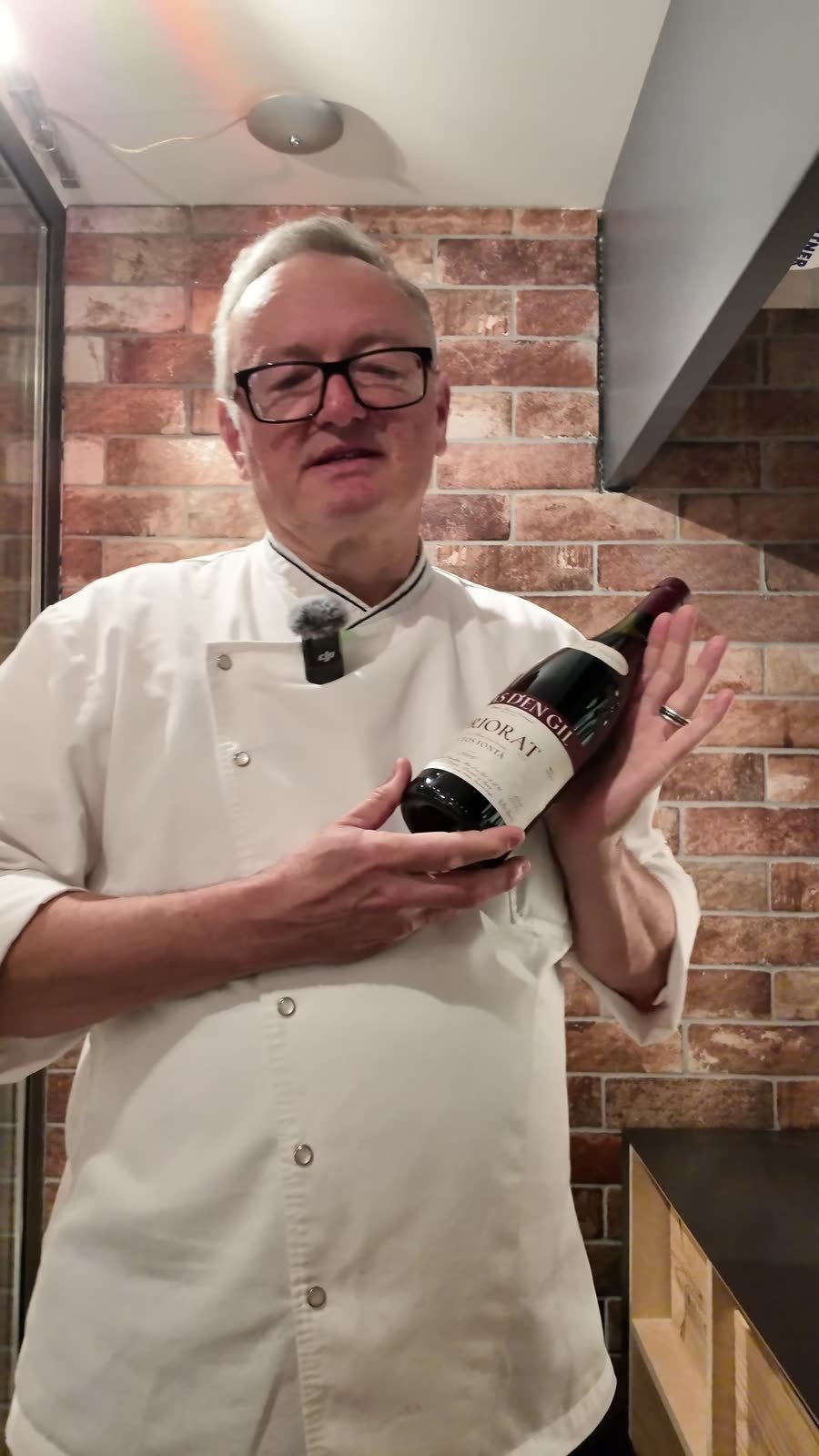 Gastgeber Albi von Felten hält eine Flasche Wein vor der Backsteinwand der Suite.